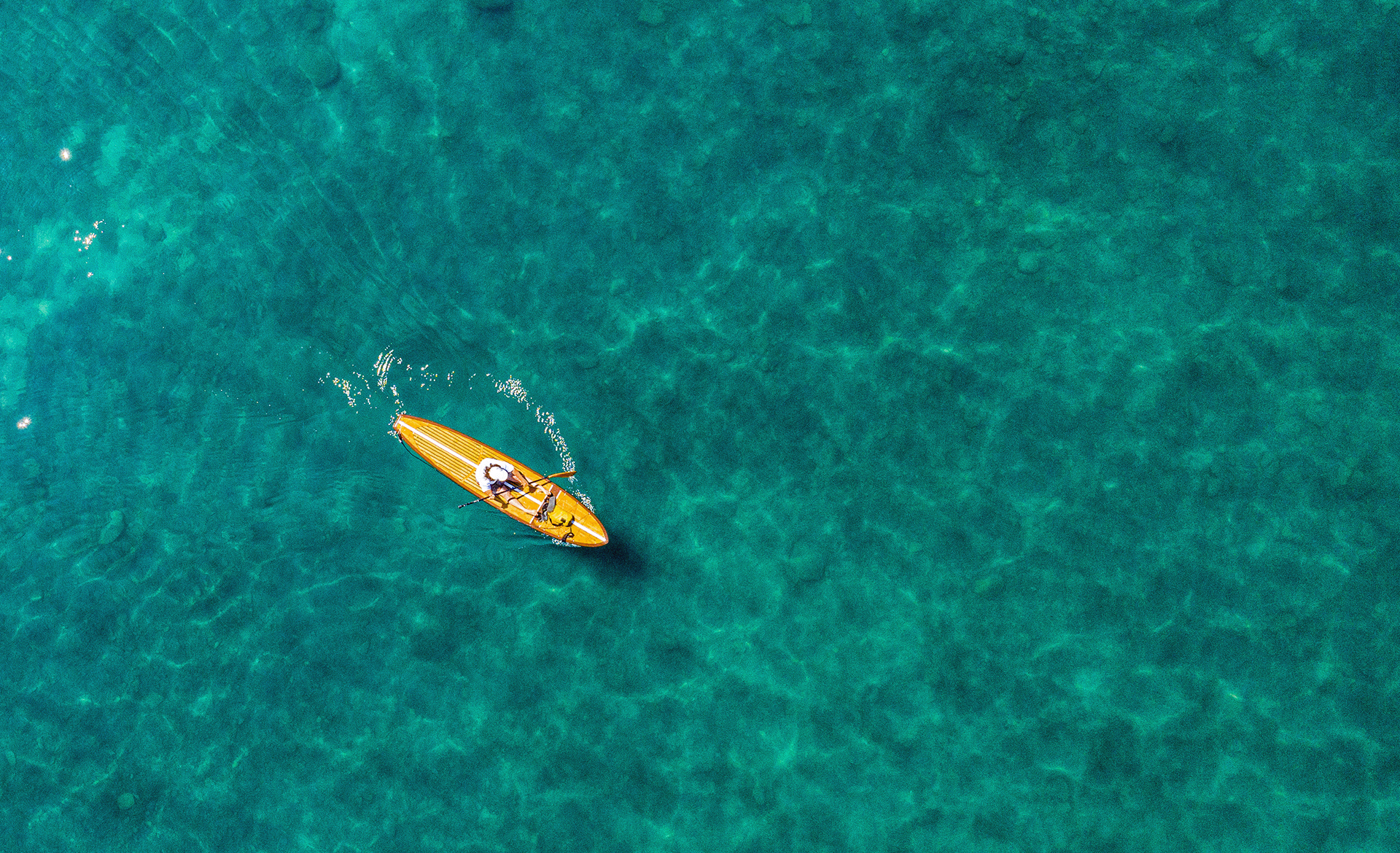 birds-eye view of beautiful turquoise water with a person on a wooden paddle board