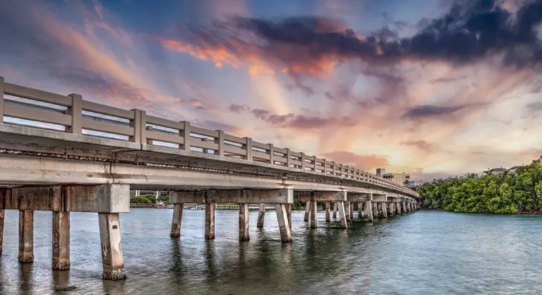 a long wodden bridge connects land with buildings in the distance over a lake