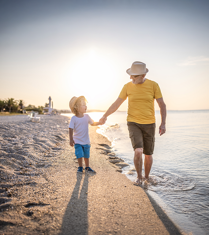 grandfather holds grandson's hand while walking on the beach at sunset